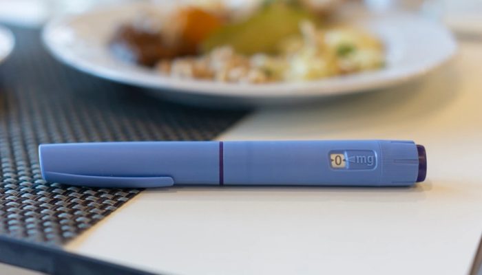 1 de 1 Uma caneta Ozempic em um guardanapo ao lado de um prato de comida não saudável, conceito...