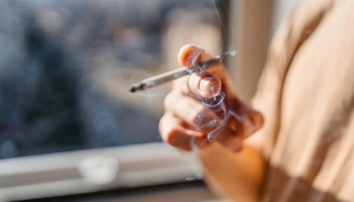 1 de 1 Close de um jovem/adolescente em pé perto da janela fumando um cigarro em casa. Metrópol...