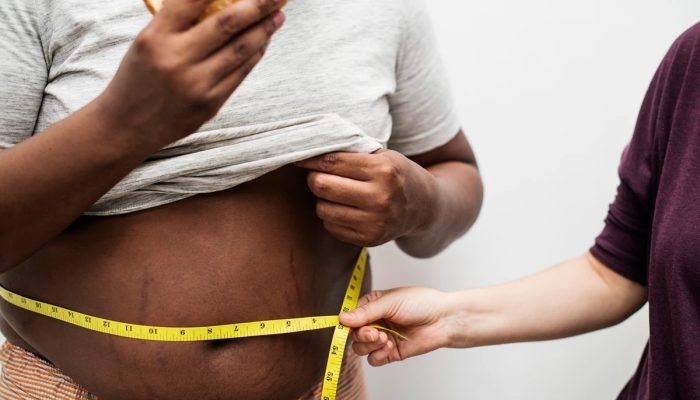 1 de 1 Foto colorida de corpo masculino segurando um hamburguer enquanto outra pessoa mede com fi...