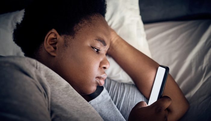 Imagem mostra mulher negra olhando o celular na cama - Entenda por que assistir vídeos acelerado...