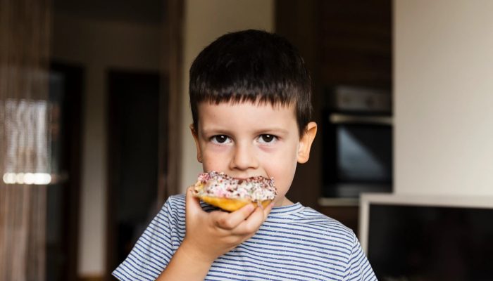 1 de 1 Foto de um menino comendo rosquinha doce em casa. Ele é branco e tem cabelo curto e preto...