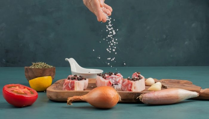1 de 1 Foto colorida de uma mão colocando sal que tempera uma tipo de carne numa tábua de madei...